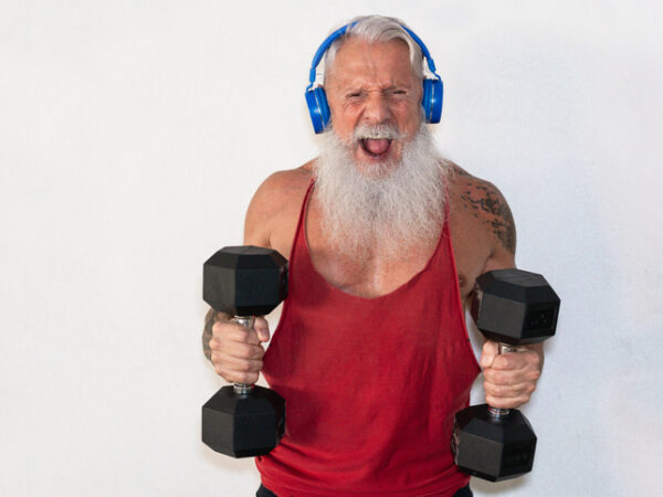Senior man doing gym workout with dumbbells while wearing a headset, presumably listening to music