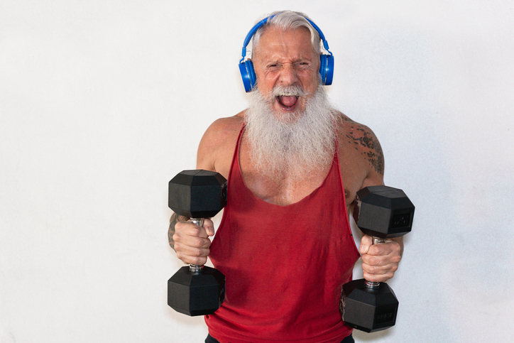 Senior man doing gym workout with dumbbells while wearing a headset, presumably listening to music