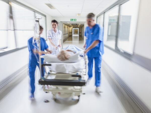 medical staff pushing an older adult on a gurney in a hospital