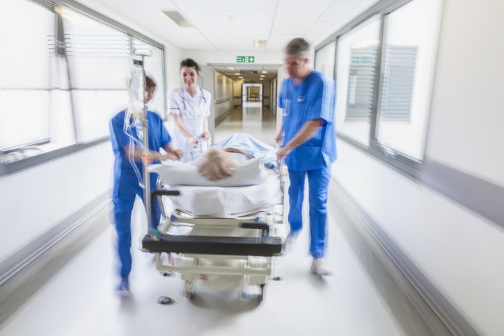 medical staff pushing an older adult on a gurney in a hospital