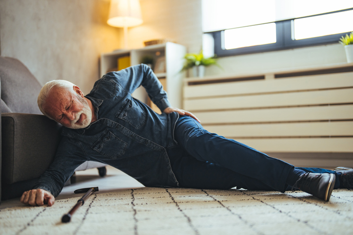 Older male adult laying on the floor clutching his hip