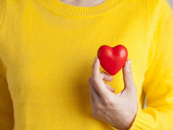 Woman wearing a bright yellow sweater holding a red heart up to her chest