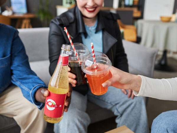 Close up shot of fizzy drinks in plastic cups each being held by three friends