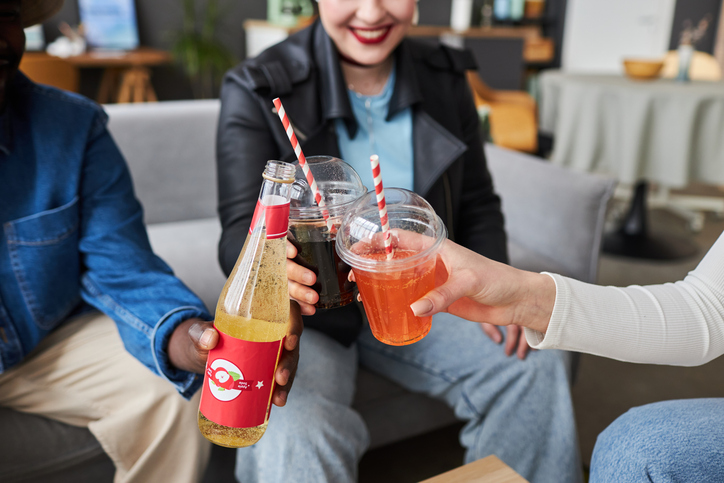 Close up shot of fizzy drinks in plastic cups each being held by three friends